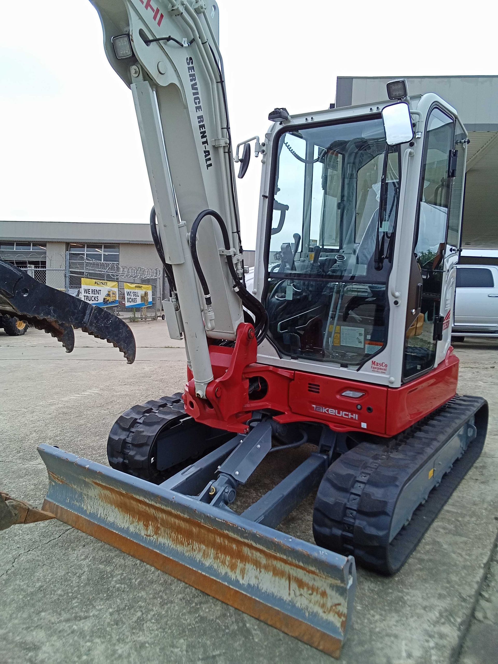 A compact, white and red excavator with tracks and a blade, parked on concrete.