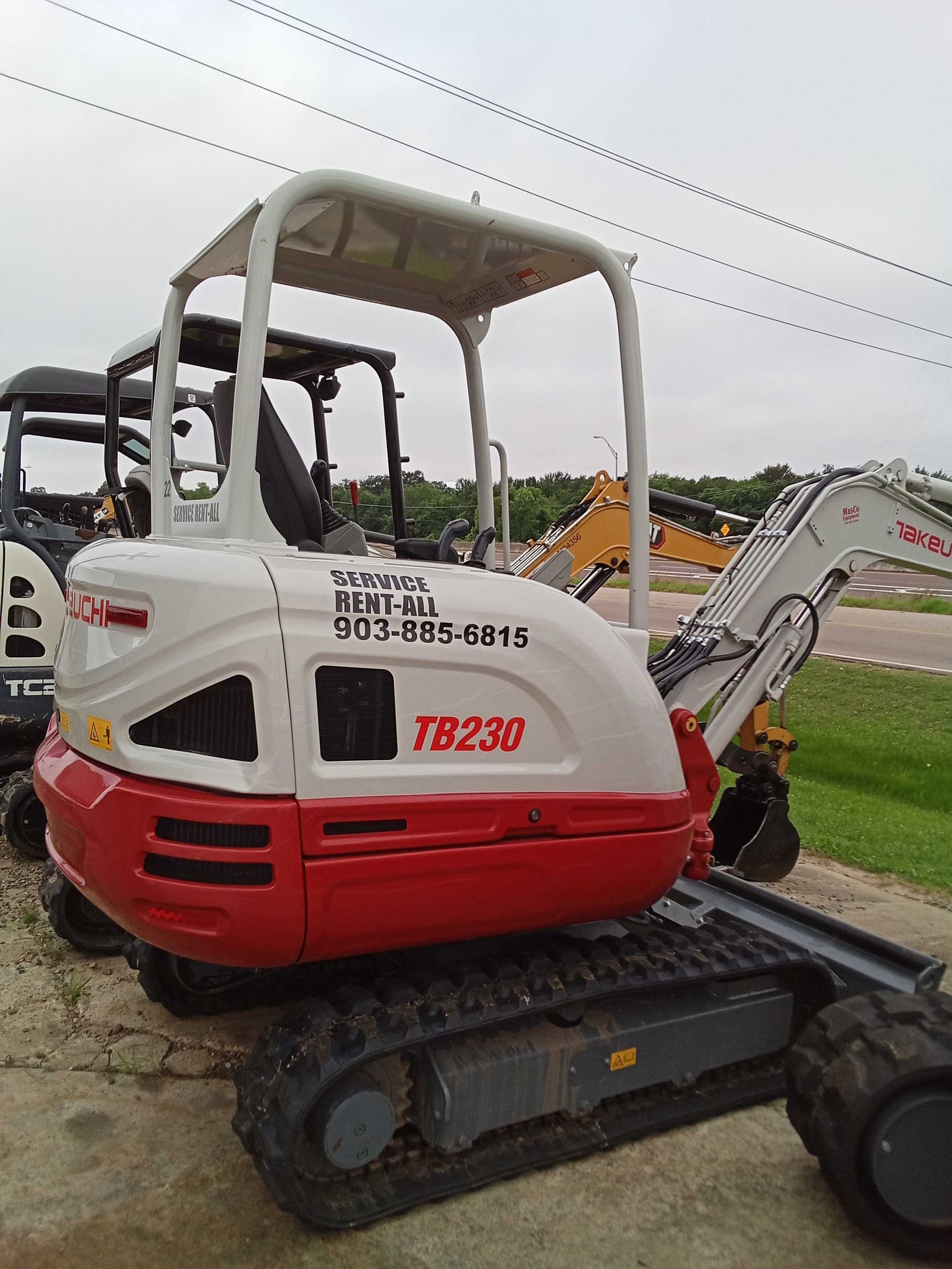 Mini excavator, white and red, parked outdoors.