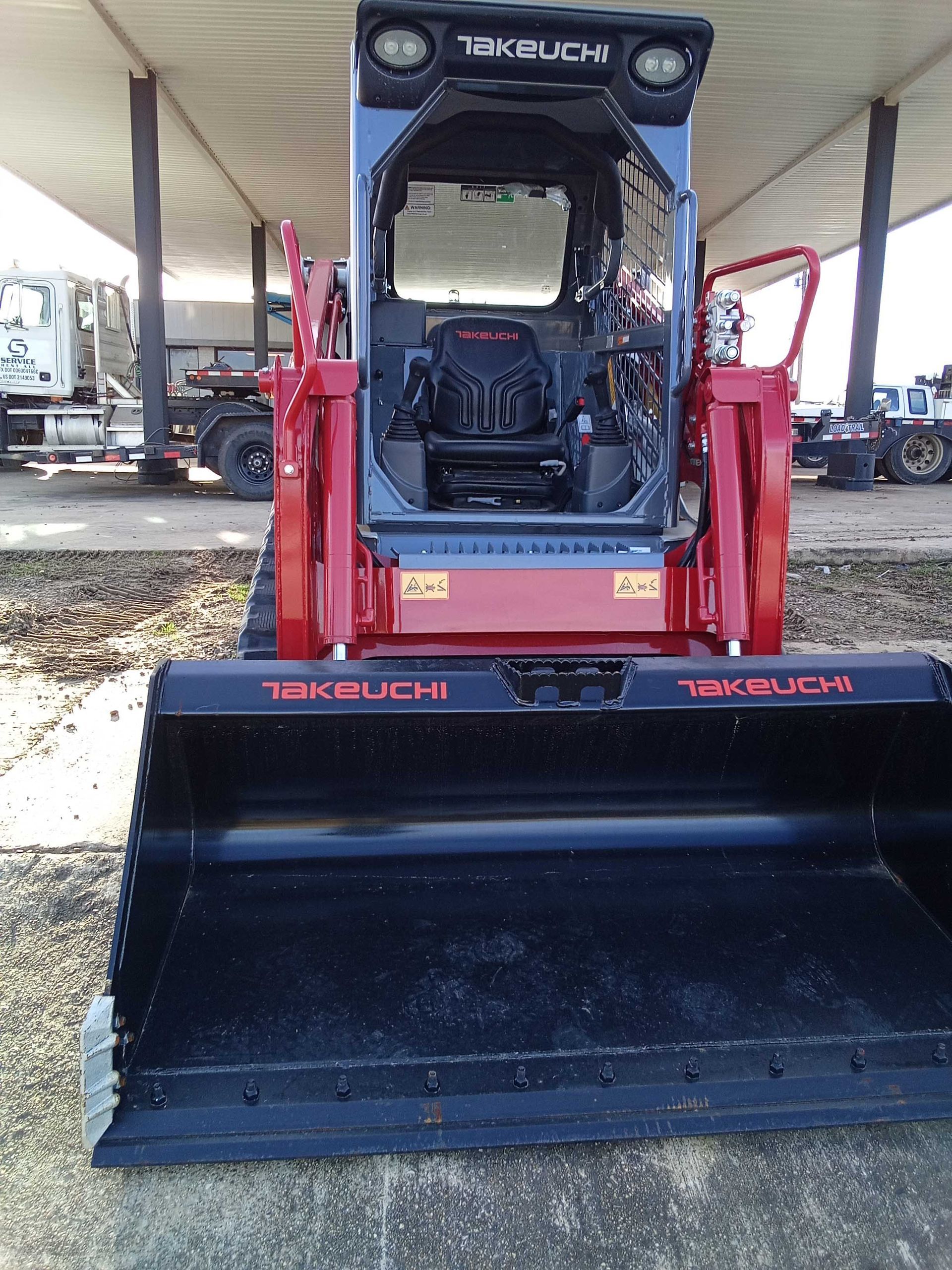 Red and black Takeuchi compact track loader with bucket, parked outdoors under a shelter.