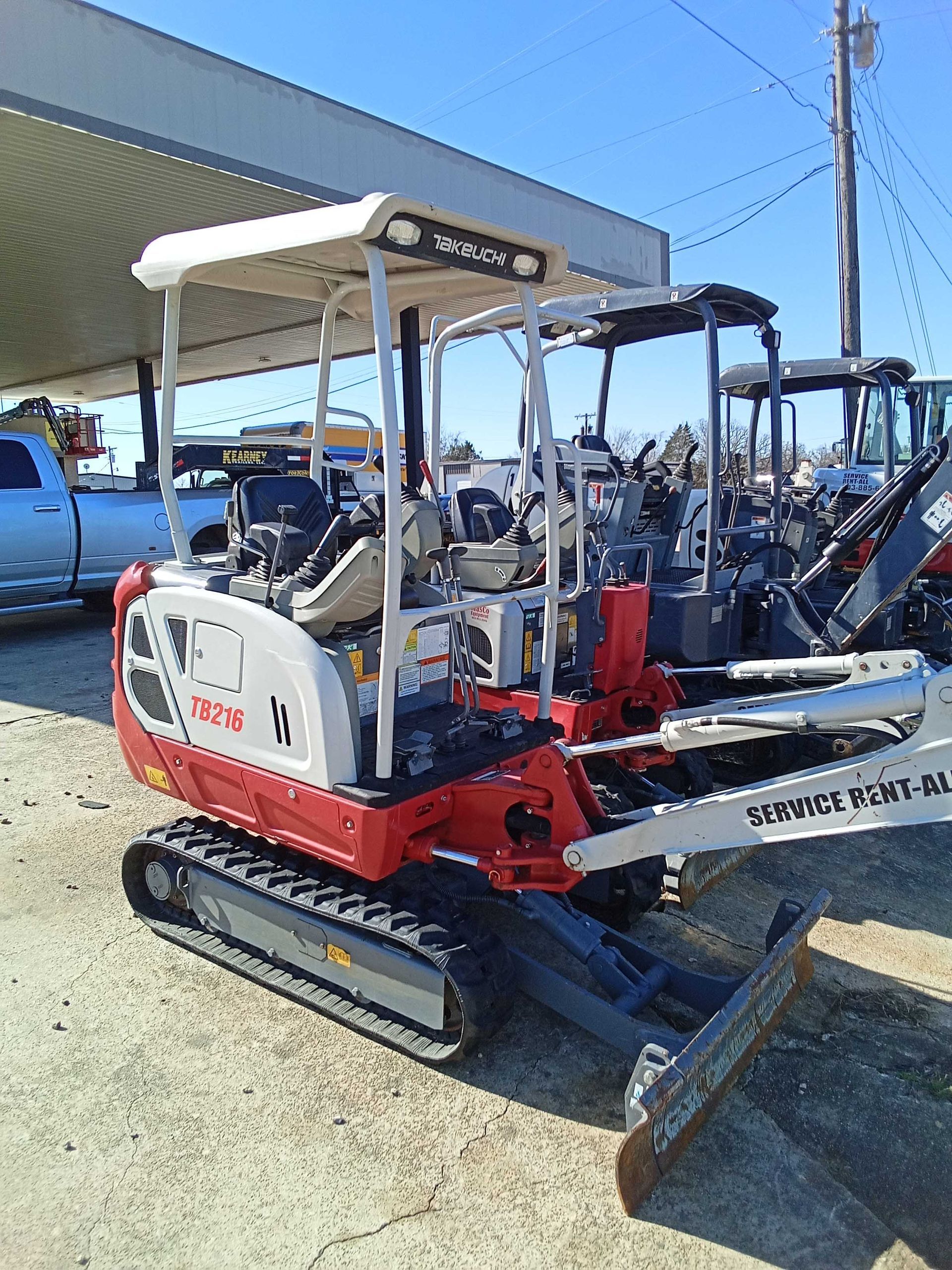 Red and white mini excavator with protective canopy, parked outside on a sunny day.