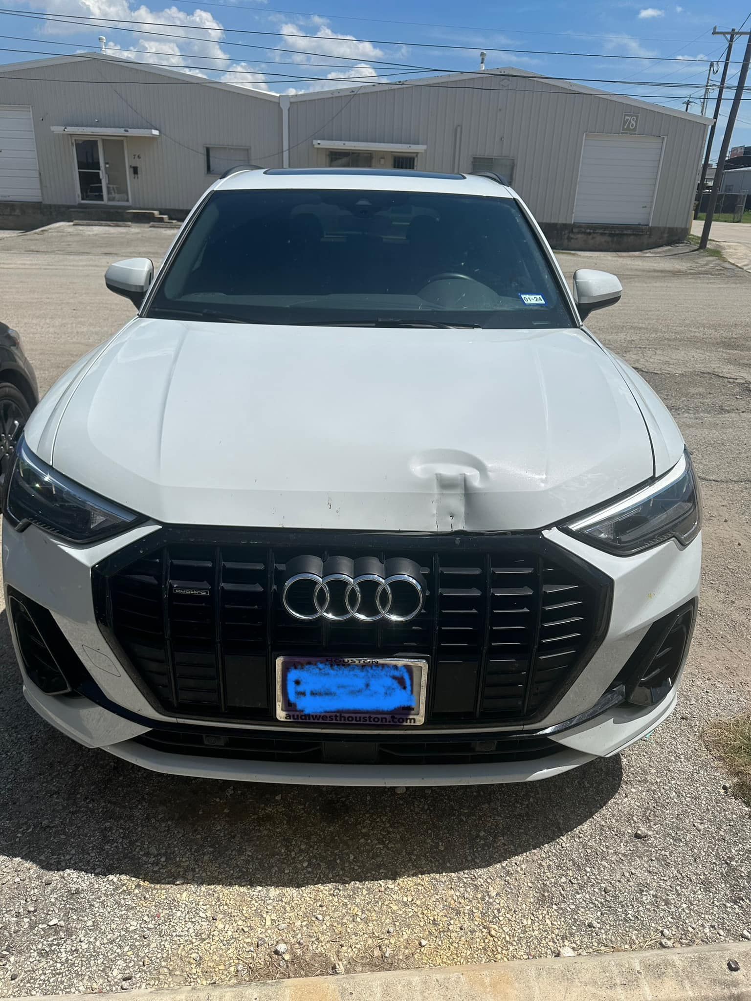 A white audi q8 is parked in a gravel lot in front of a building.