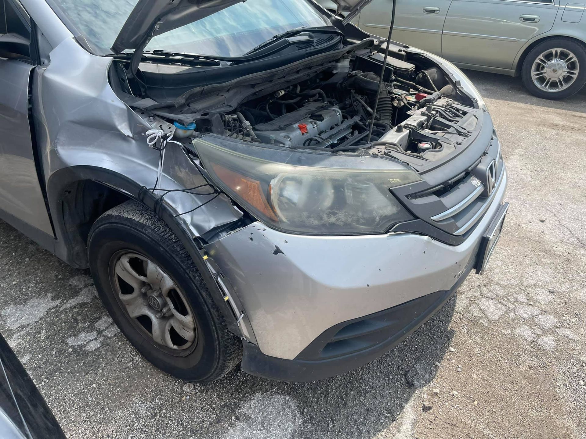 A silver car with the hood up is parked in a parking lot.
