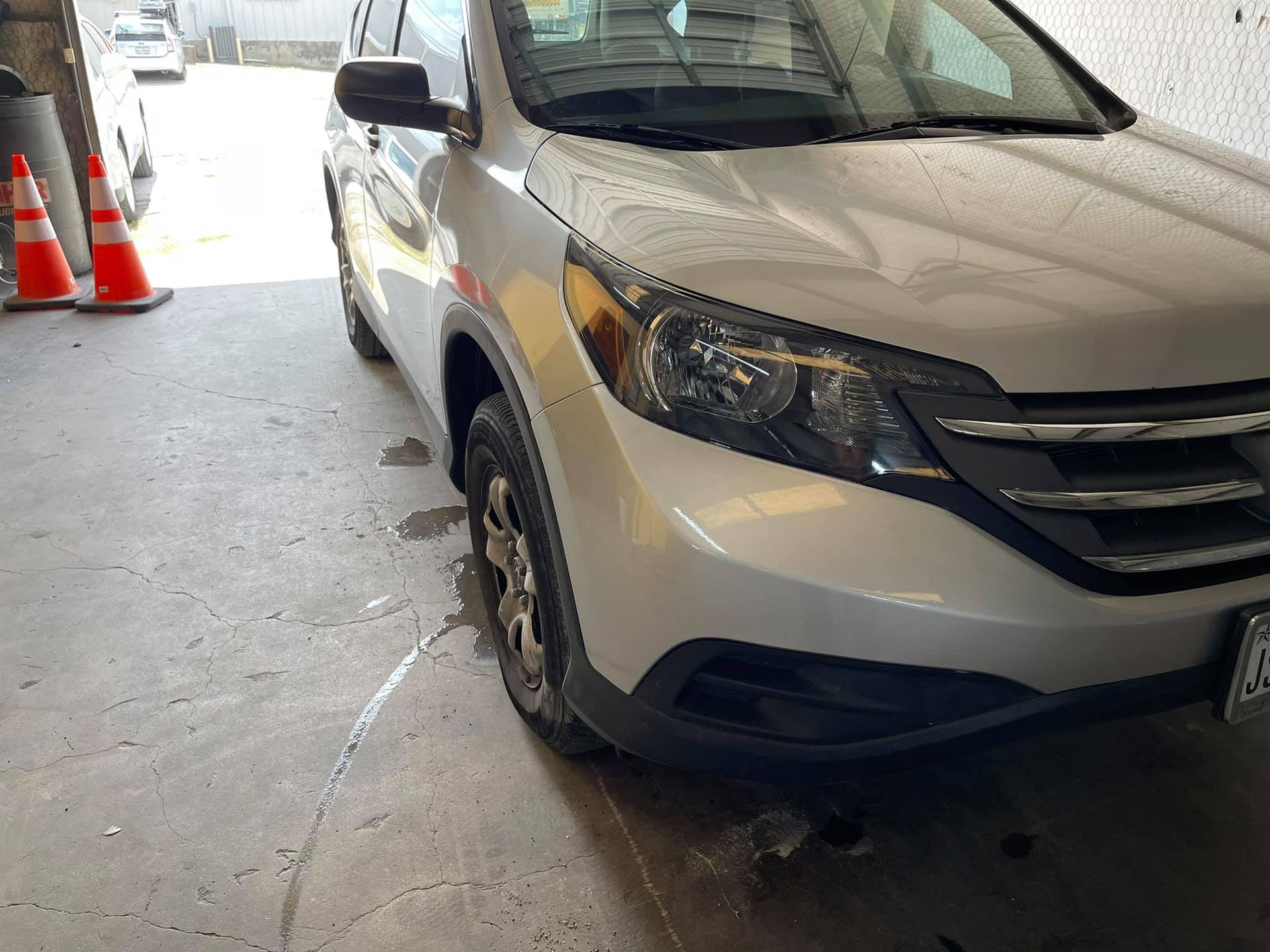 A white car is parked in a garage next to traffic cones.