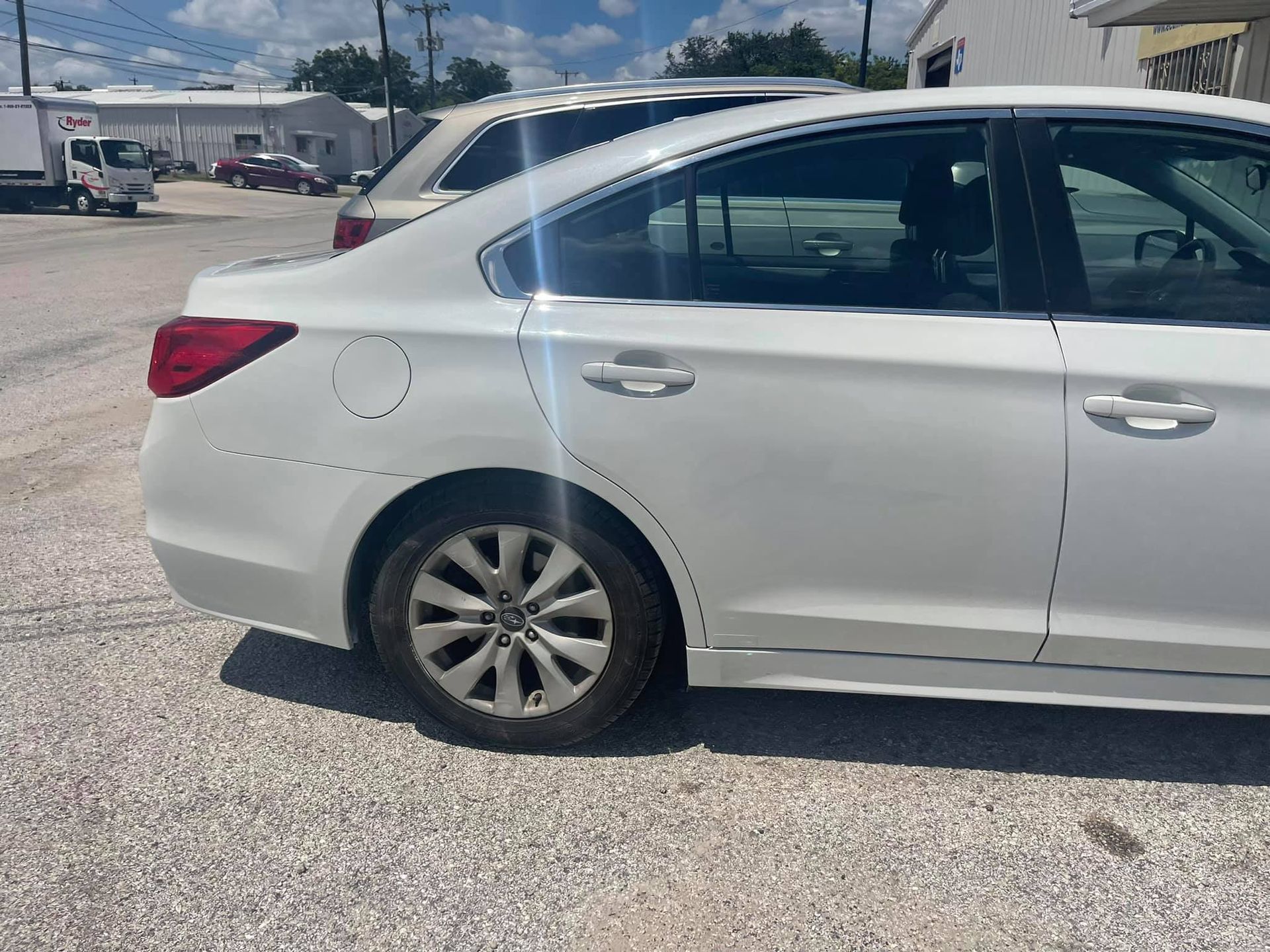 A white car is parked in a gravel lot.