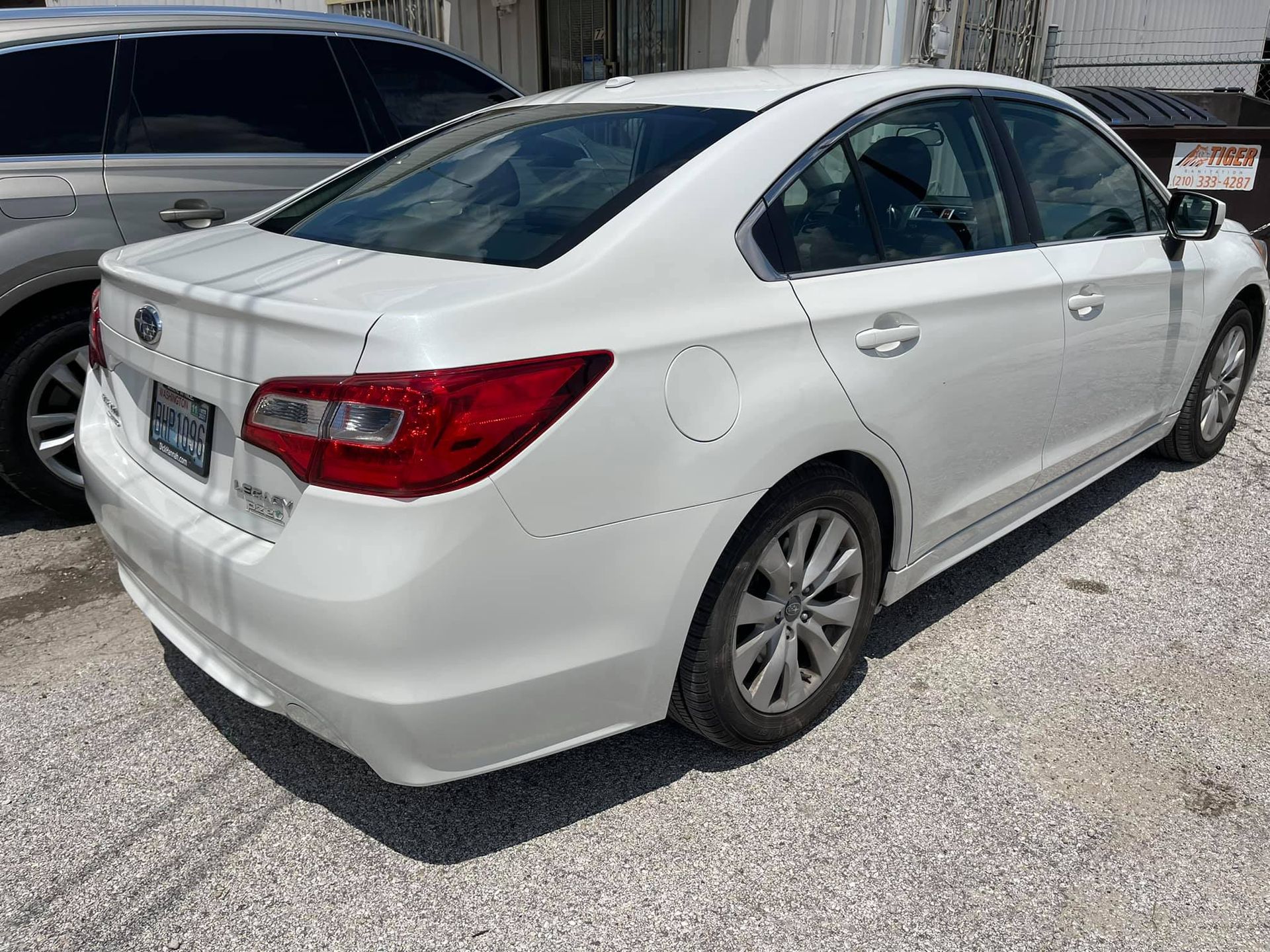 A white subaru legacy is parked in a gravel lot.