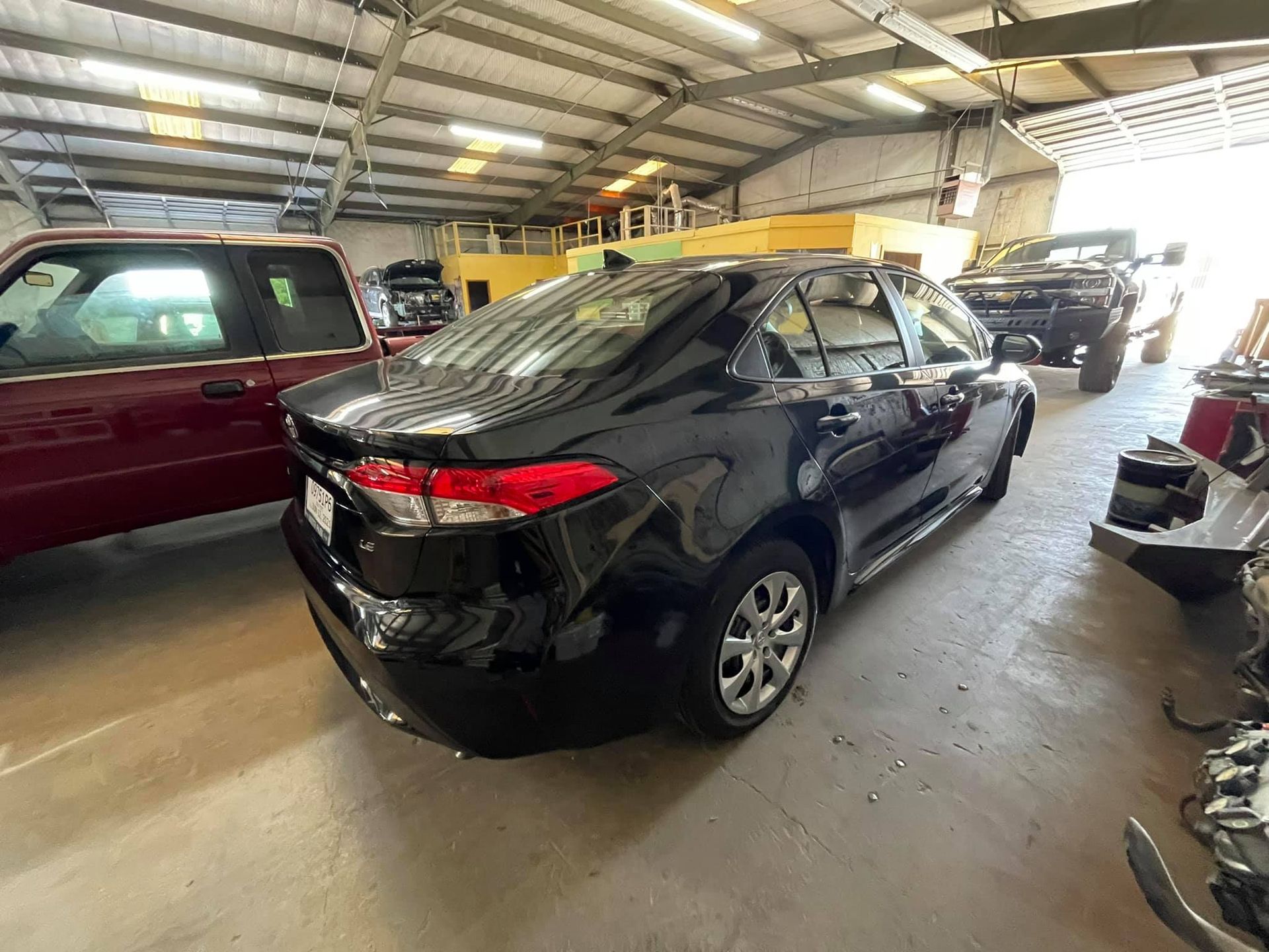 A black car is parked in a garage next to a red truck.