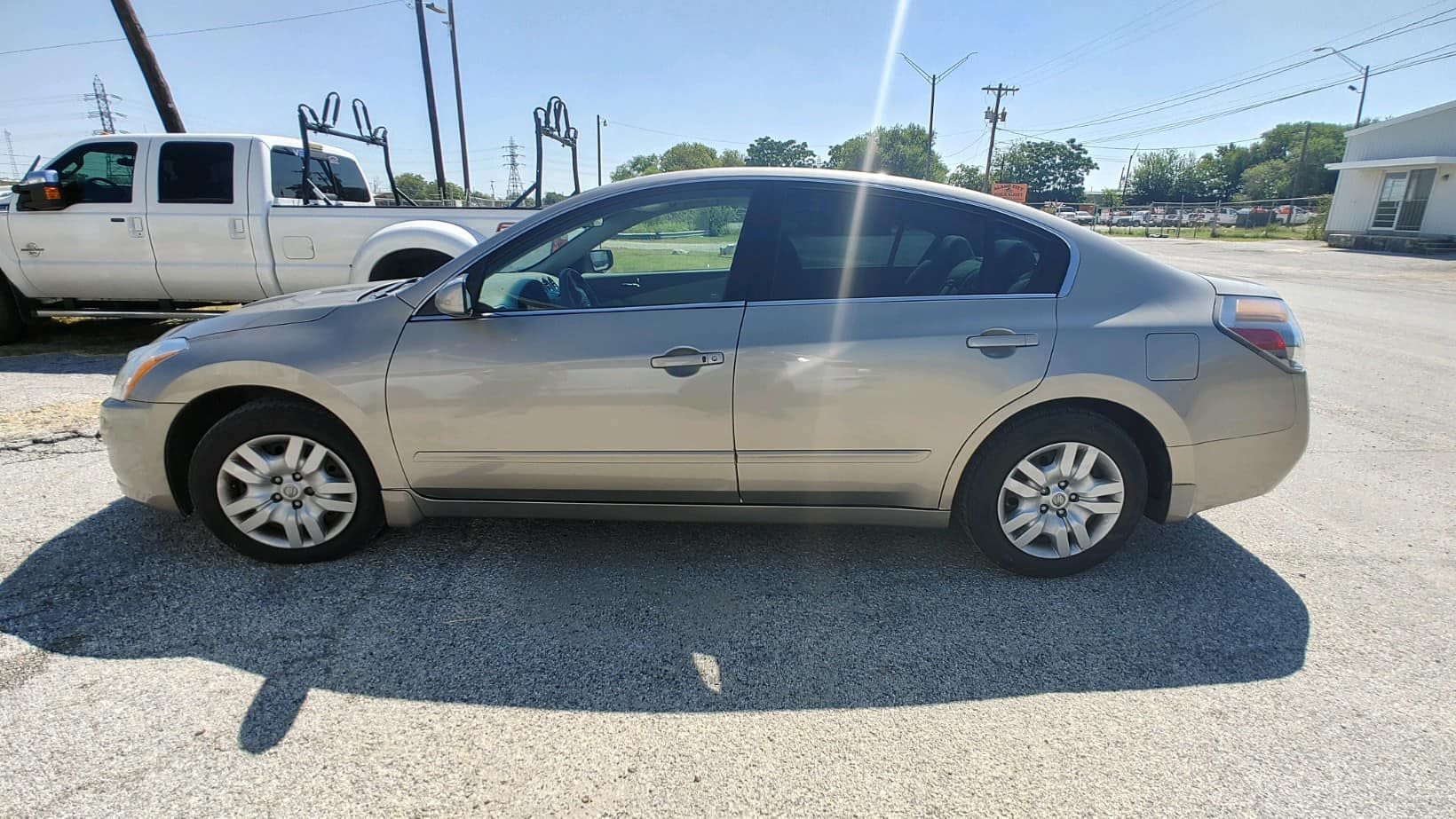A silver car is parked in a gravel lot next to a truck.