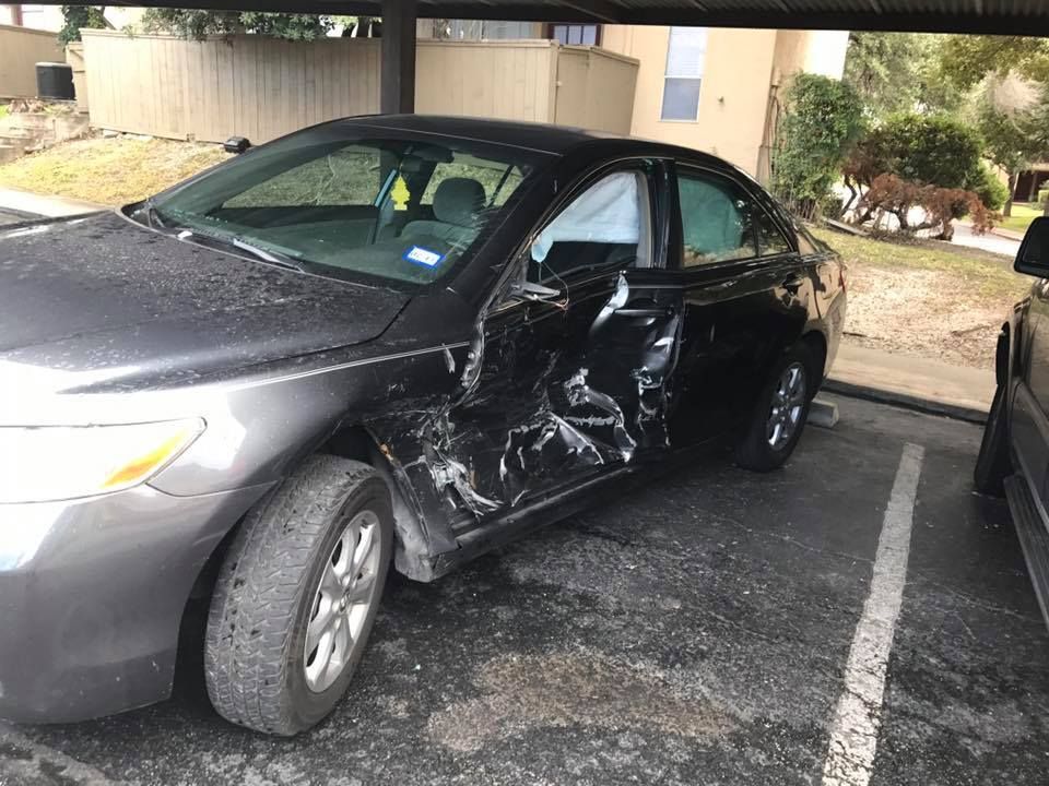 A black car with a damaged side is parked in a parking lot.