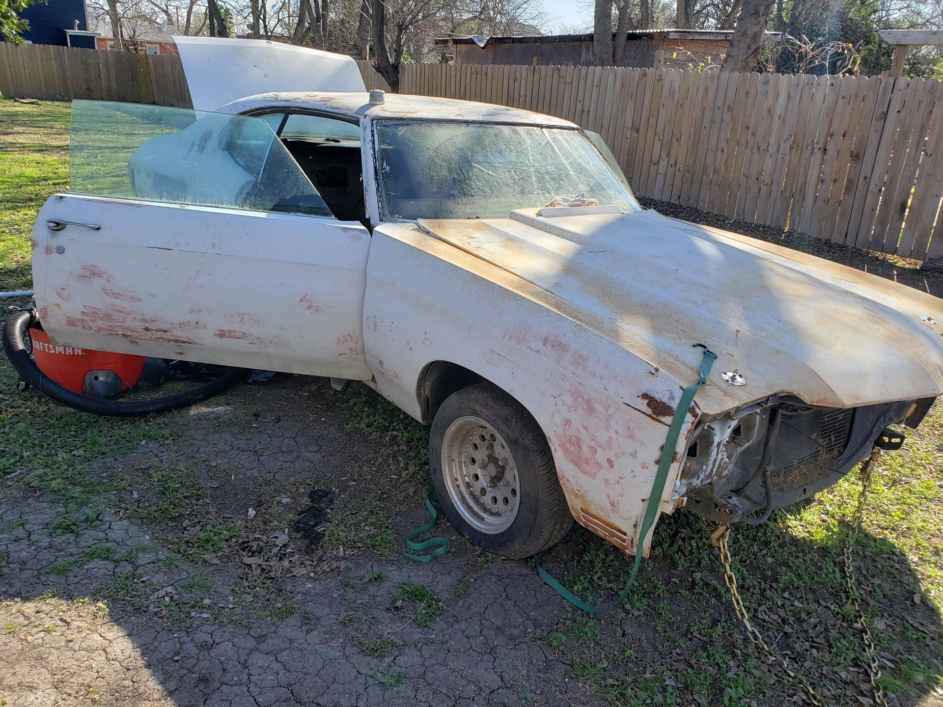 A white car is sitting in the grass with its doors open.