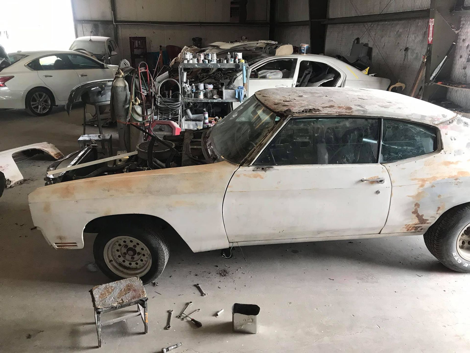 A white car is sitting in a garage with the hood open.