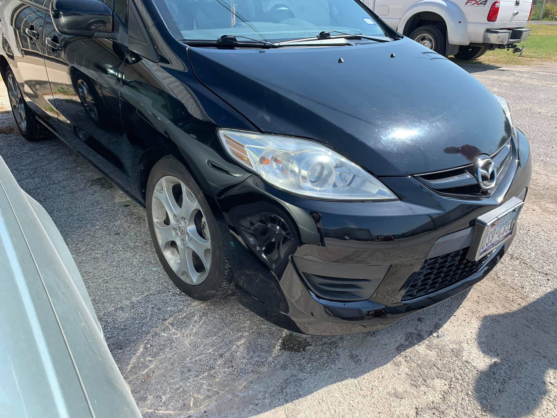 A black mazda 5 is parked in a gravel lot.