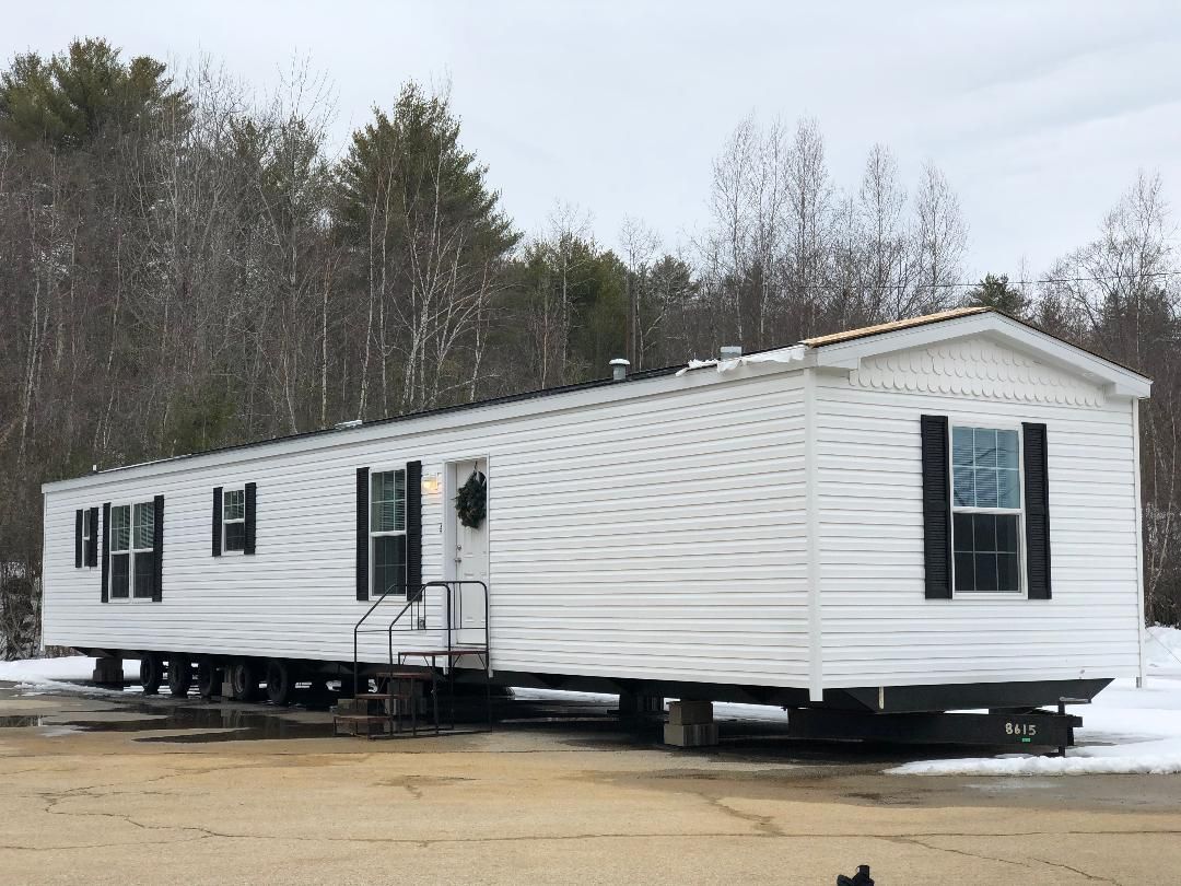 A white mobile home with black shutters is parked in a parking lot.