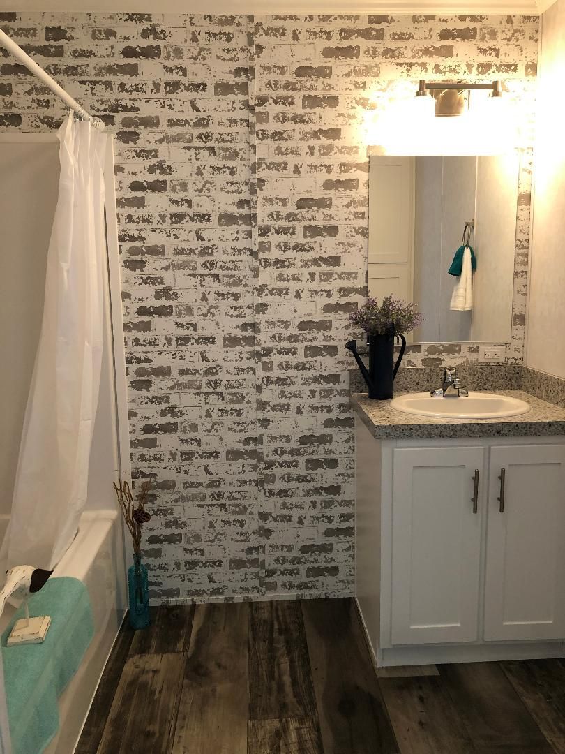 A bathroom with a sink , shower , and brick wall.