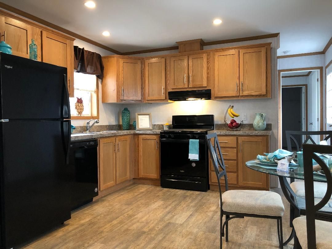 A kitchen with wooden cabinets , a black refrigerator , a stove , and a table.