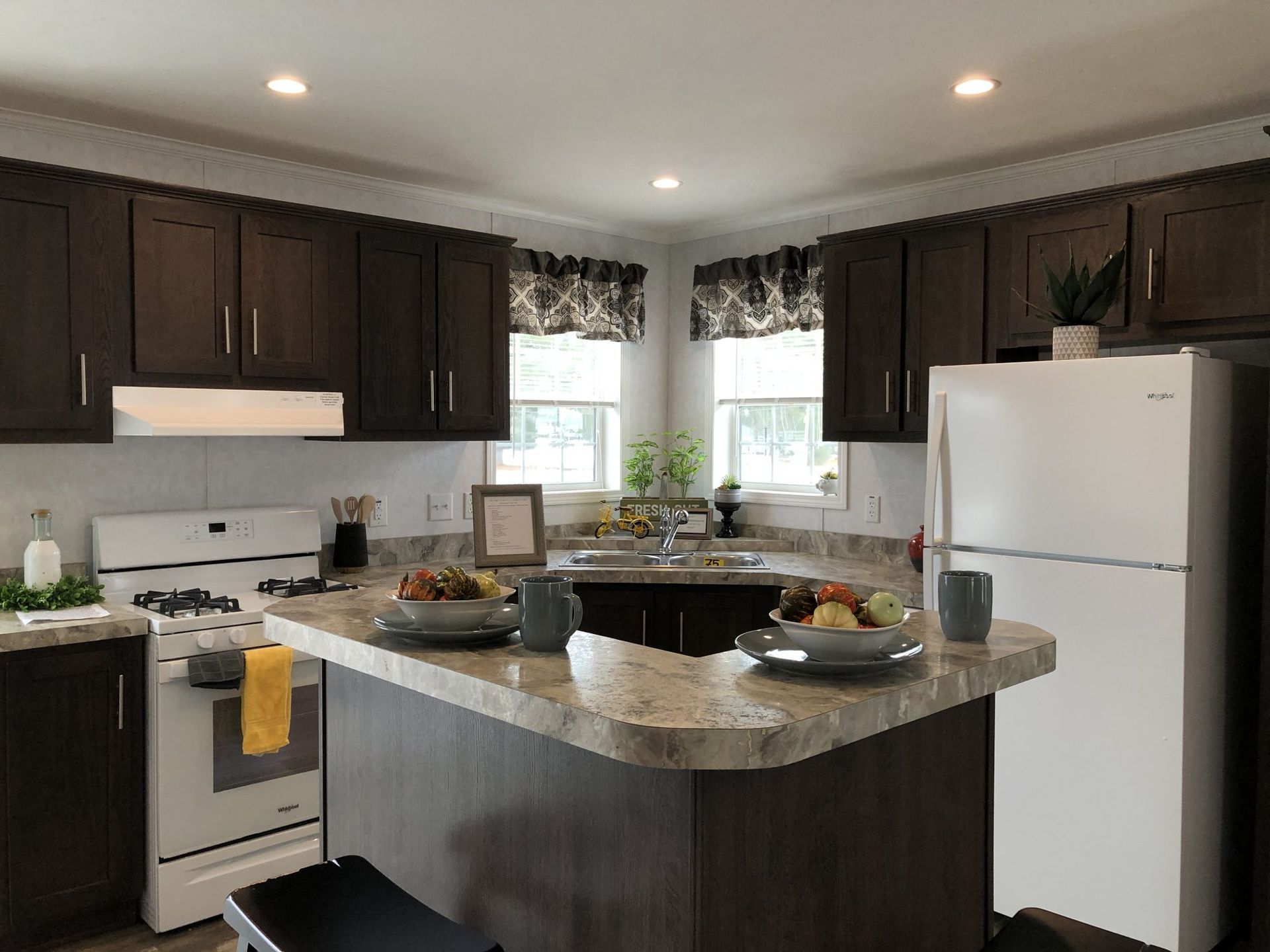 A kitchen with brown cabinets , a white refrigerator , a stove , and a large island.