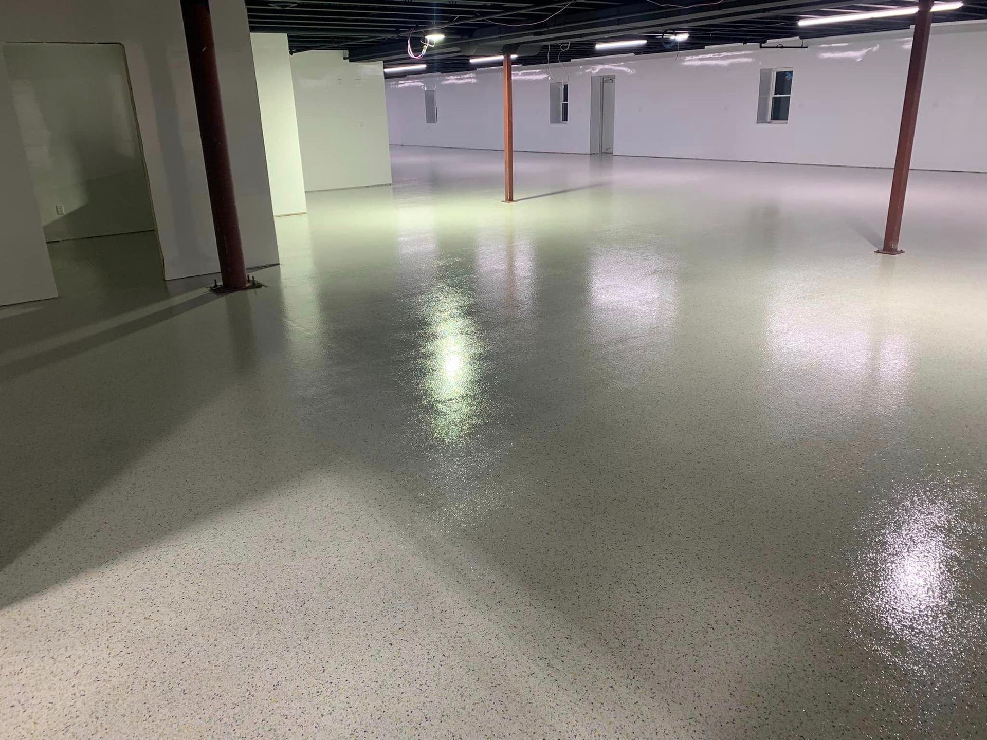 Empty basement room with glossy speckled floor and red support columns