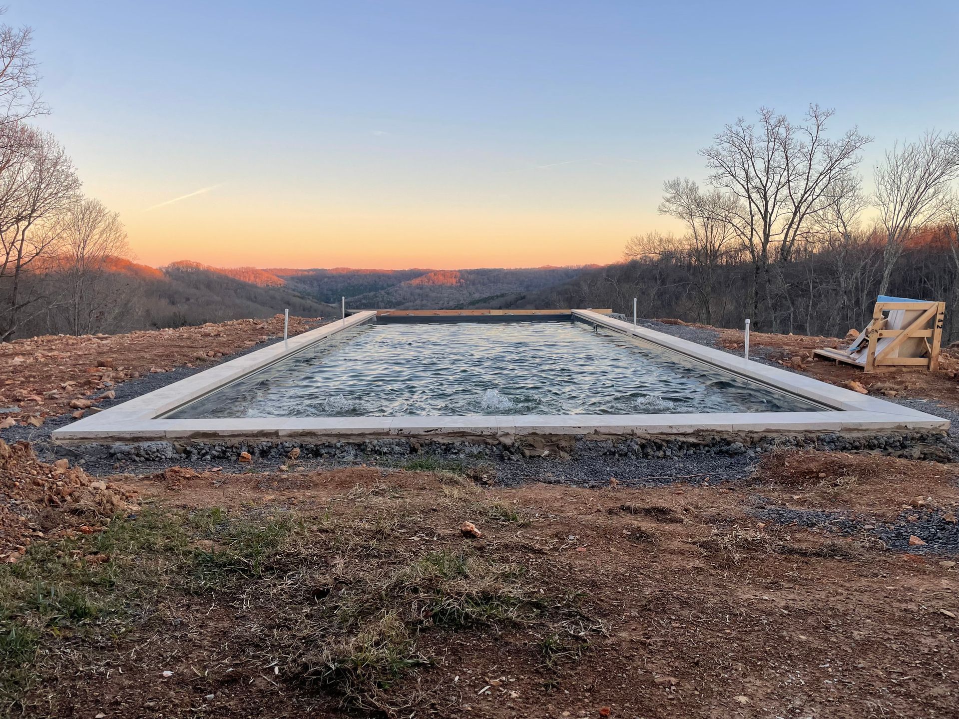 a large swimming pool is sitting on top of a dirt hill.
