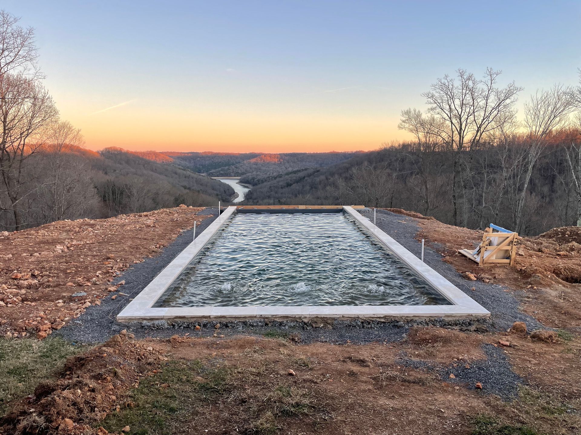 a large swimming pool is sitting on top of a hill overlooking a river.