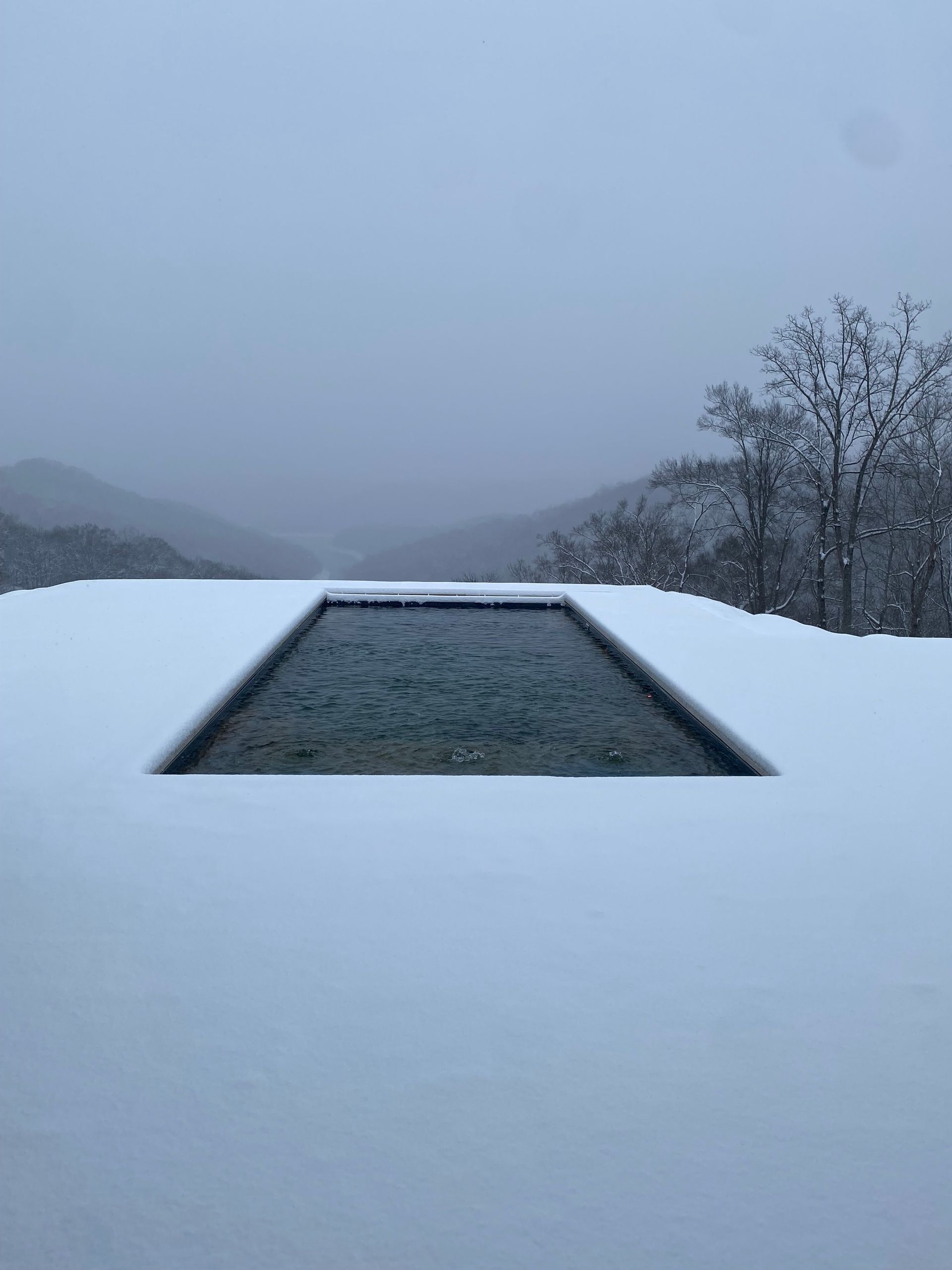 a swimming pool covered in snow with mountains in the background