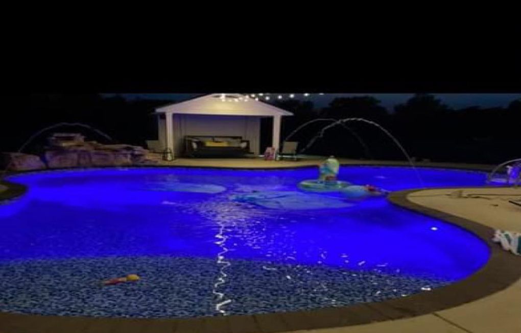 a large swimming pool is lit up with blue lights at night