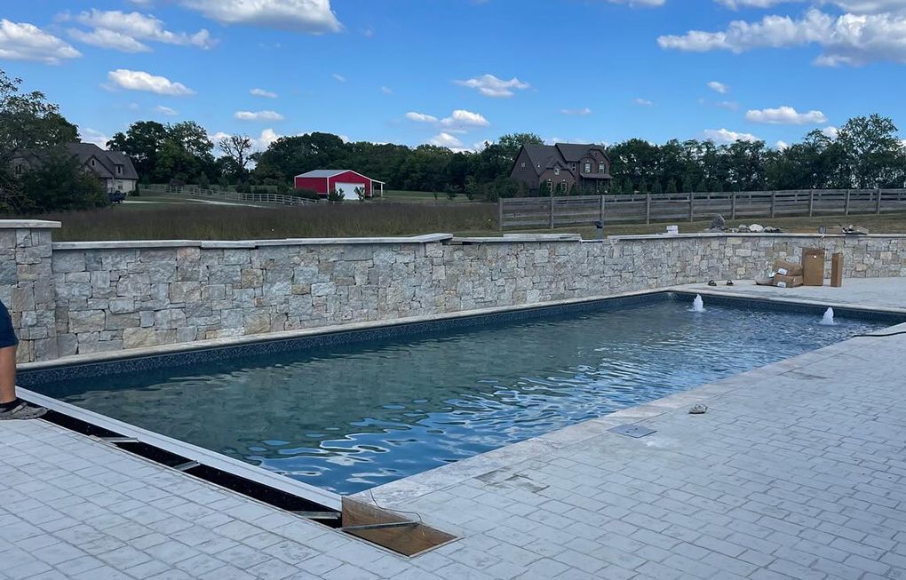 a large swimming pool with a stone wall and a red barn in the background