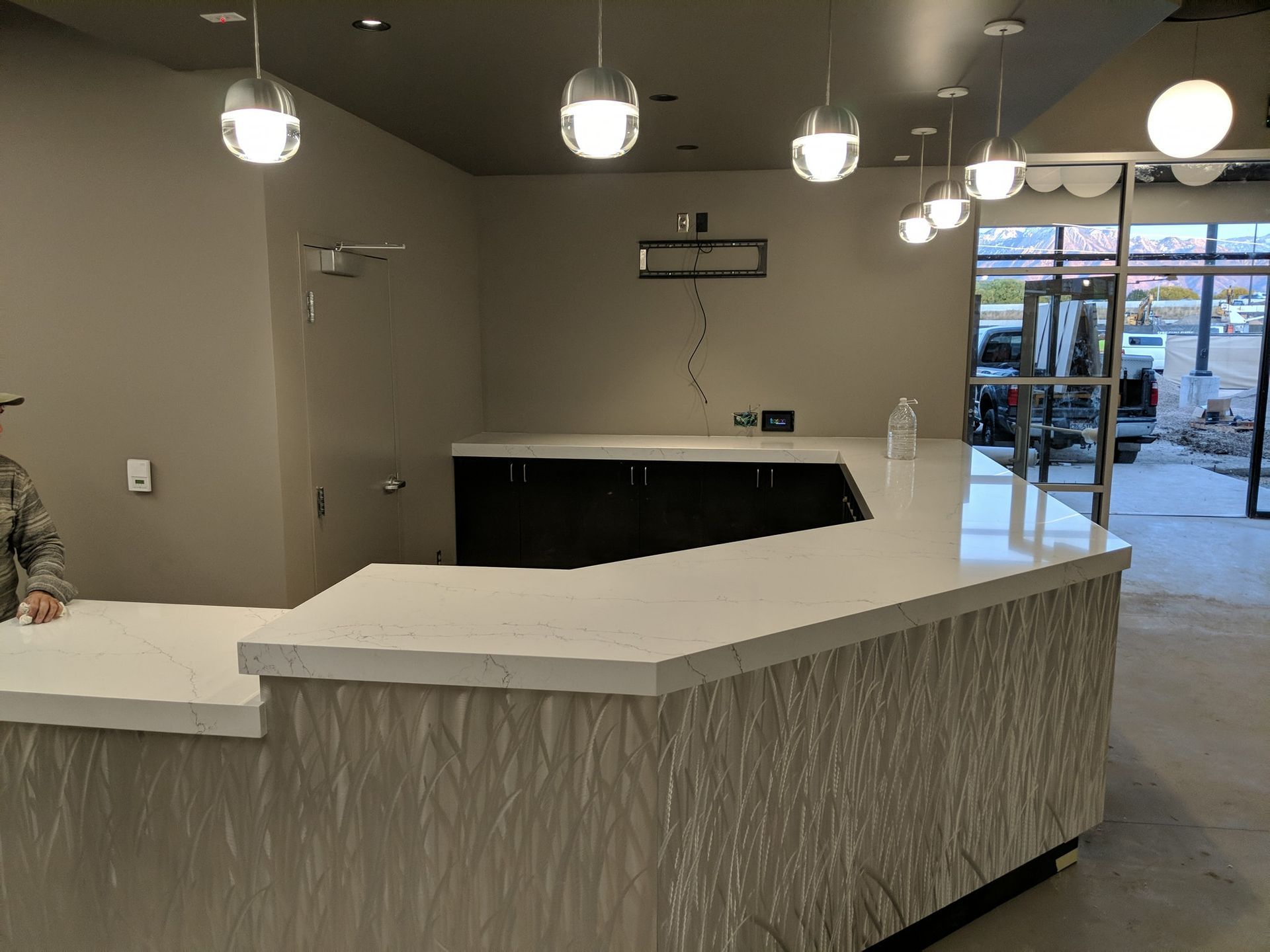 A light-colored, textured counter with cabinets and overhead globe lights in a commercial interior.