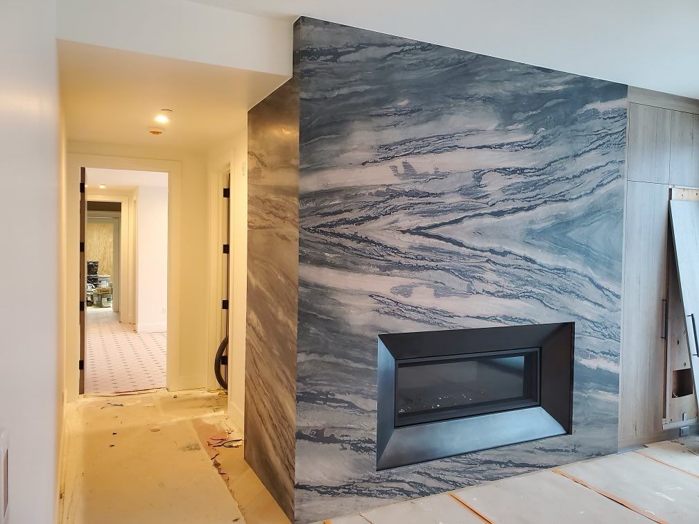 Stone fireplace with black surround, adjacent hallway. Blue-gray and white stone walls.  Hallway has open doorway.