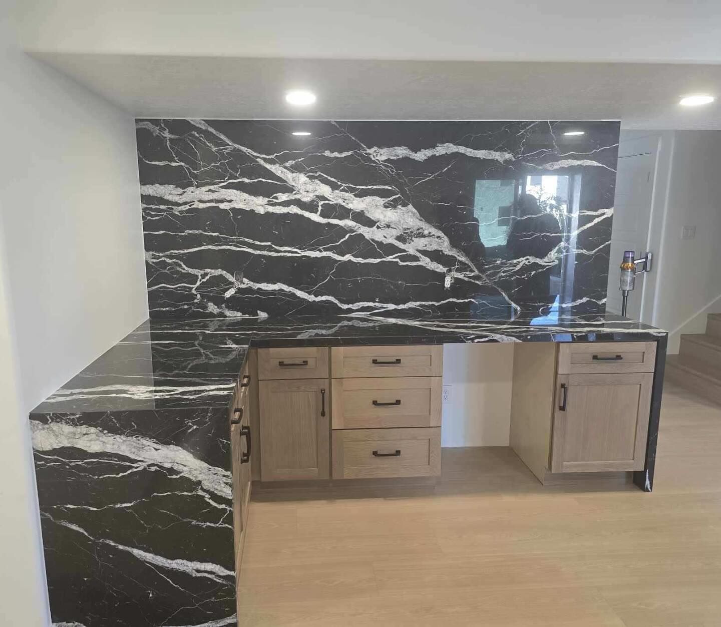 Bar with black and white marble countertop and backsplash, wooden cabinets, and recessed lighting.