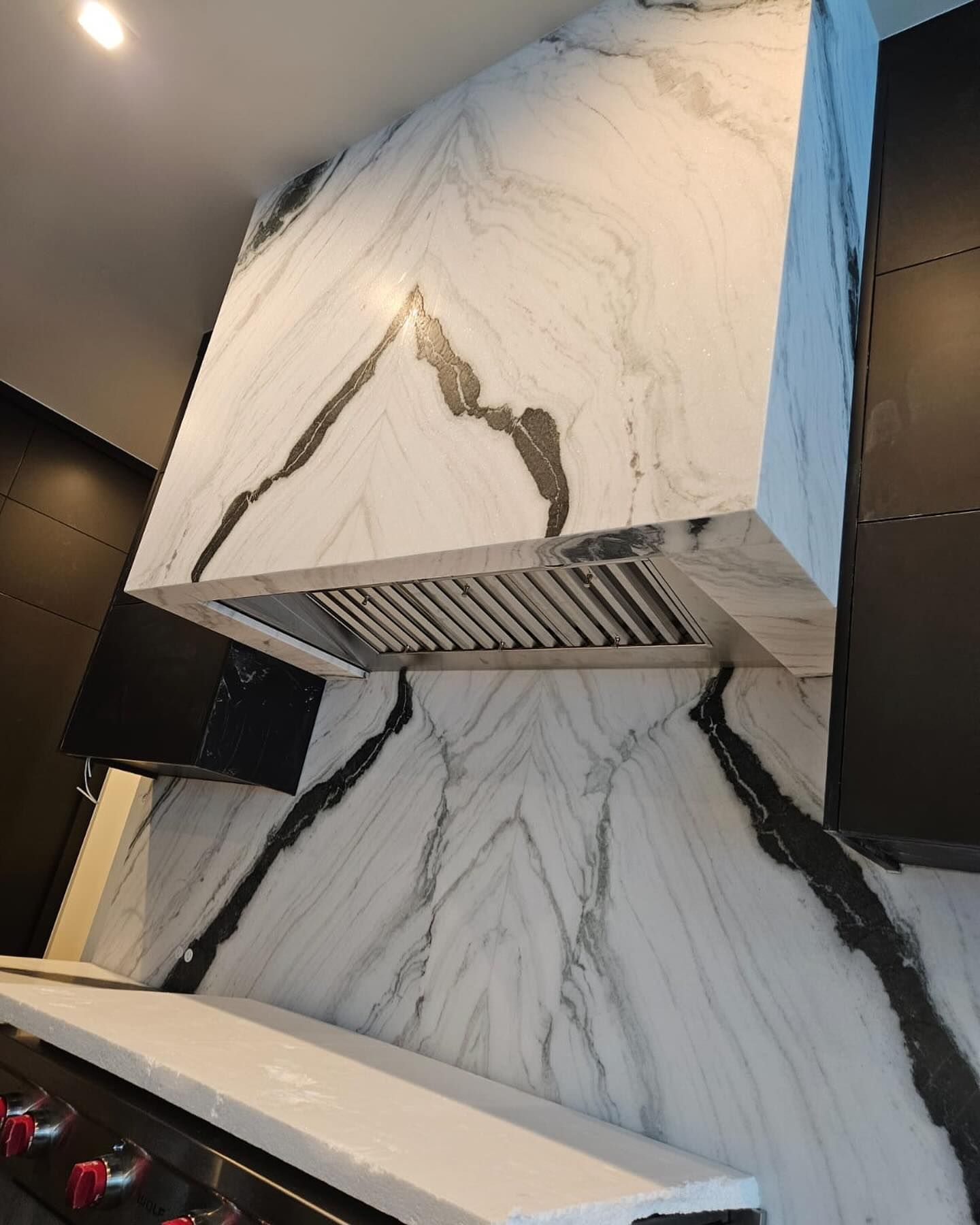 White marble kitchen range hood and backsplash with gray veining. Stainless steel vent.