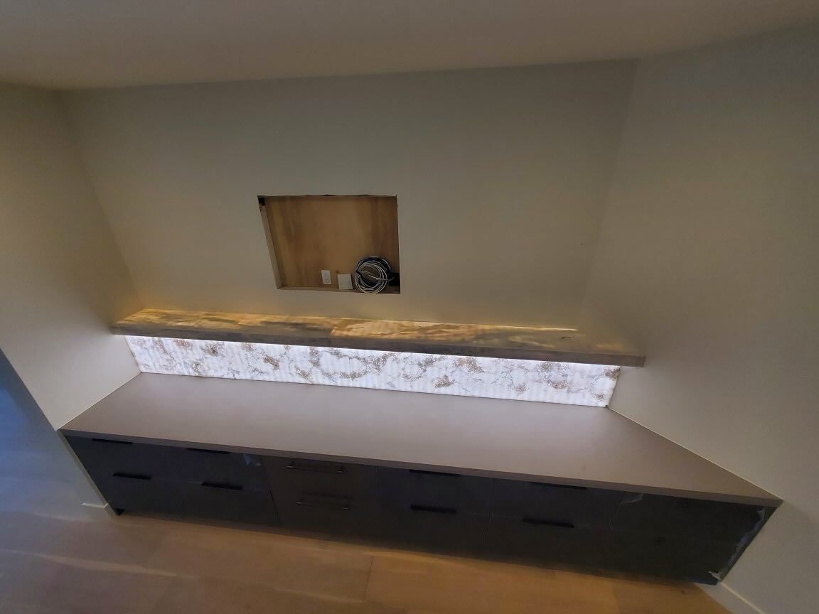 Built-in gray cabinet with a lighted countertop, a niche in the wall above, and light beige walls.