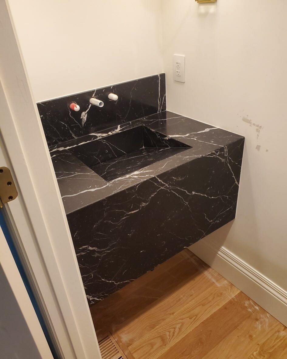 Black marble sink installed in a small bathroom with wooden flooring.