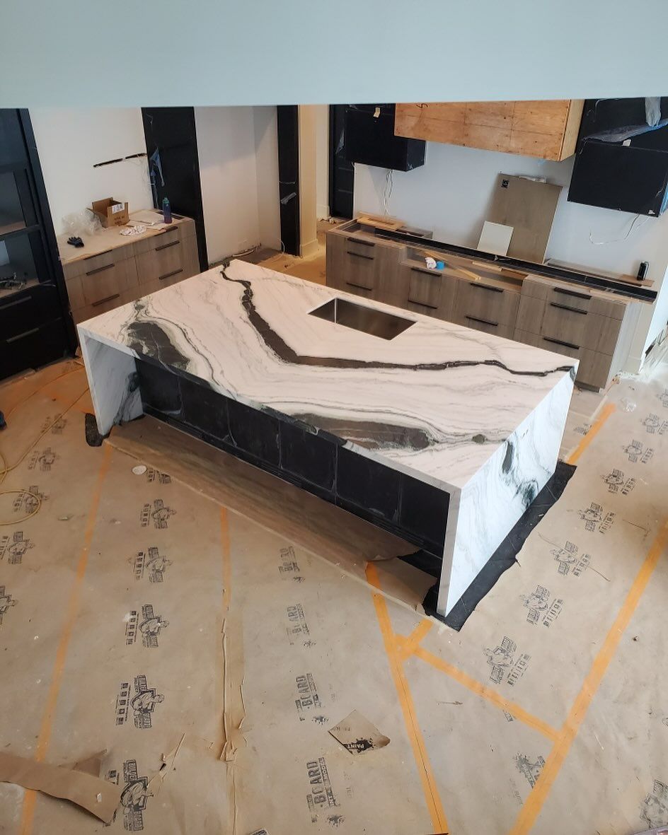 Kitchen island with white and black countertop, gray cabinets, and a sink.