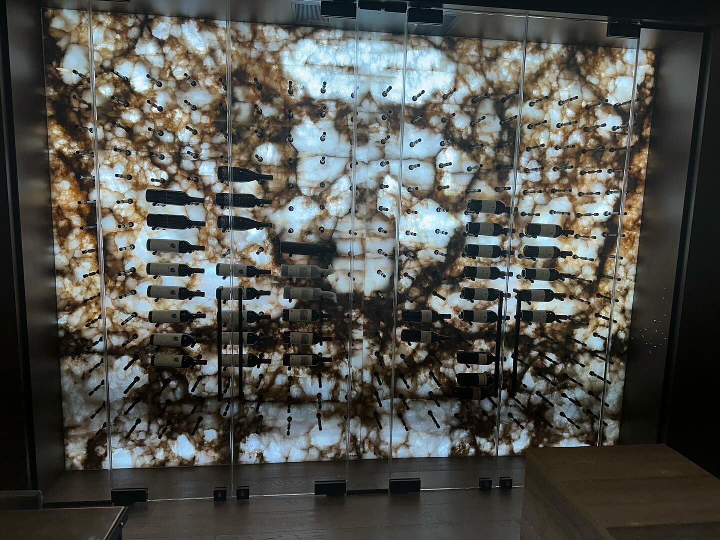 Backlit stone wine rack. Brown and white patterned stone with dark bottle holders.