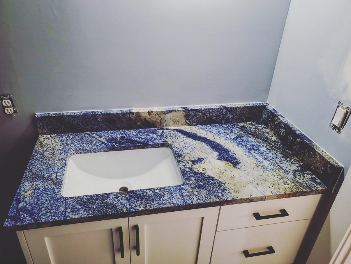 Blue and gold granite countertop with white sink, set on a white cabinet against a blue wall.