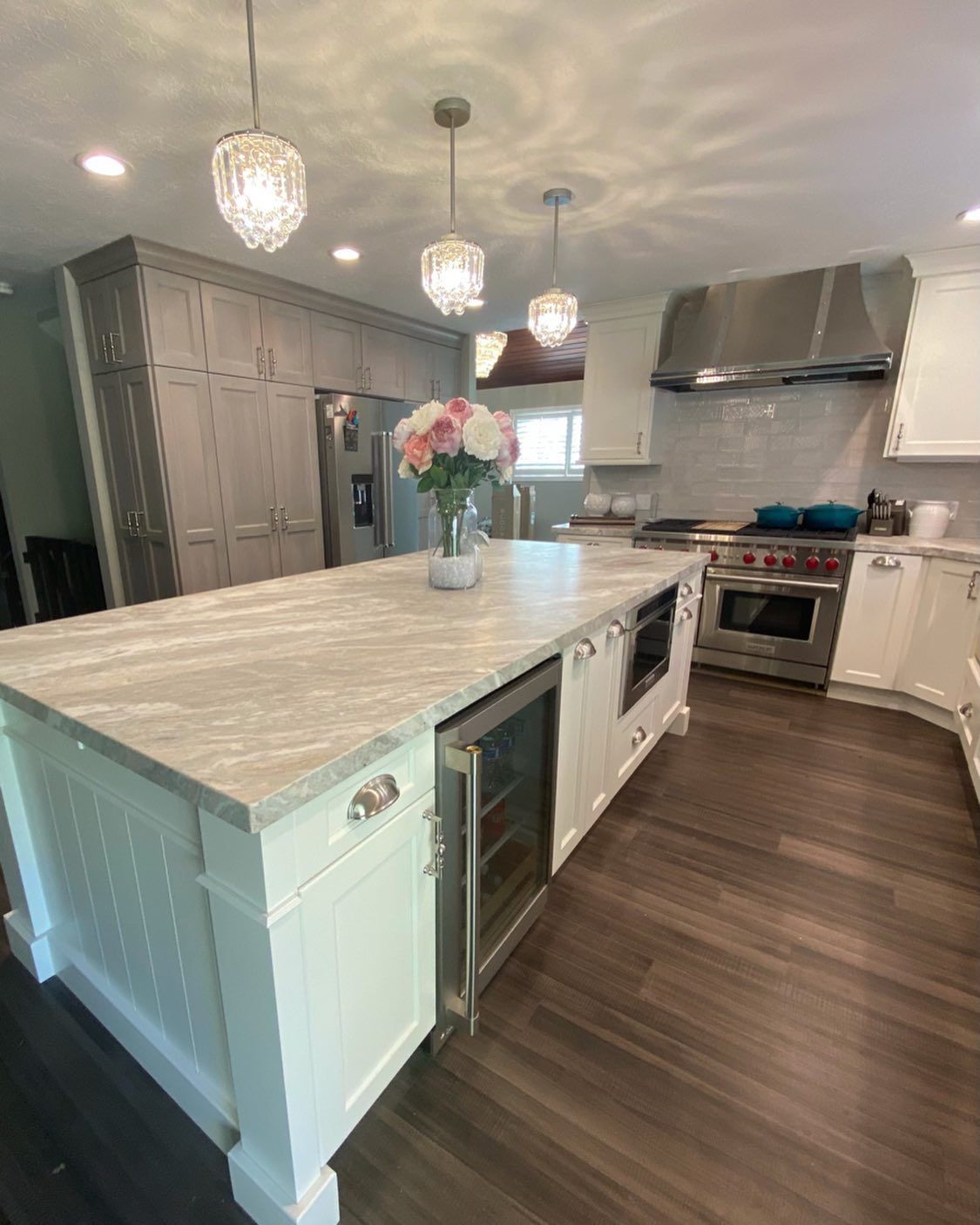 Modern kitchen with white island, gray countertop, built-in wine fridge, and pendant lights.