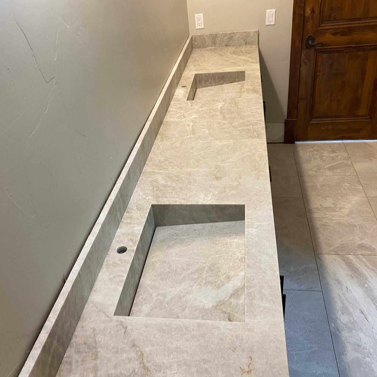 A beige marble countertop with two sink cutouts is installed in a bathroom.
