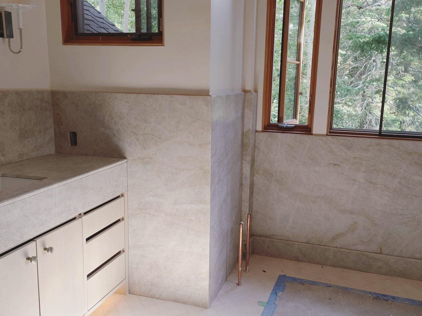 Bathroom with light countertops, cabinets, and tan tiled walls. Window and copper pipe are visible.