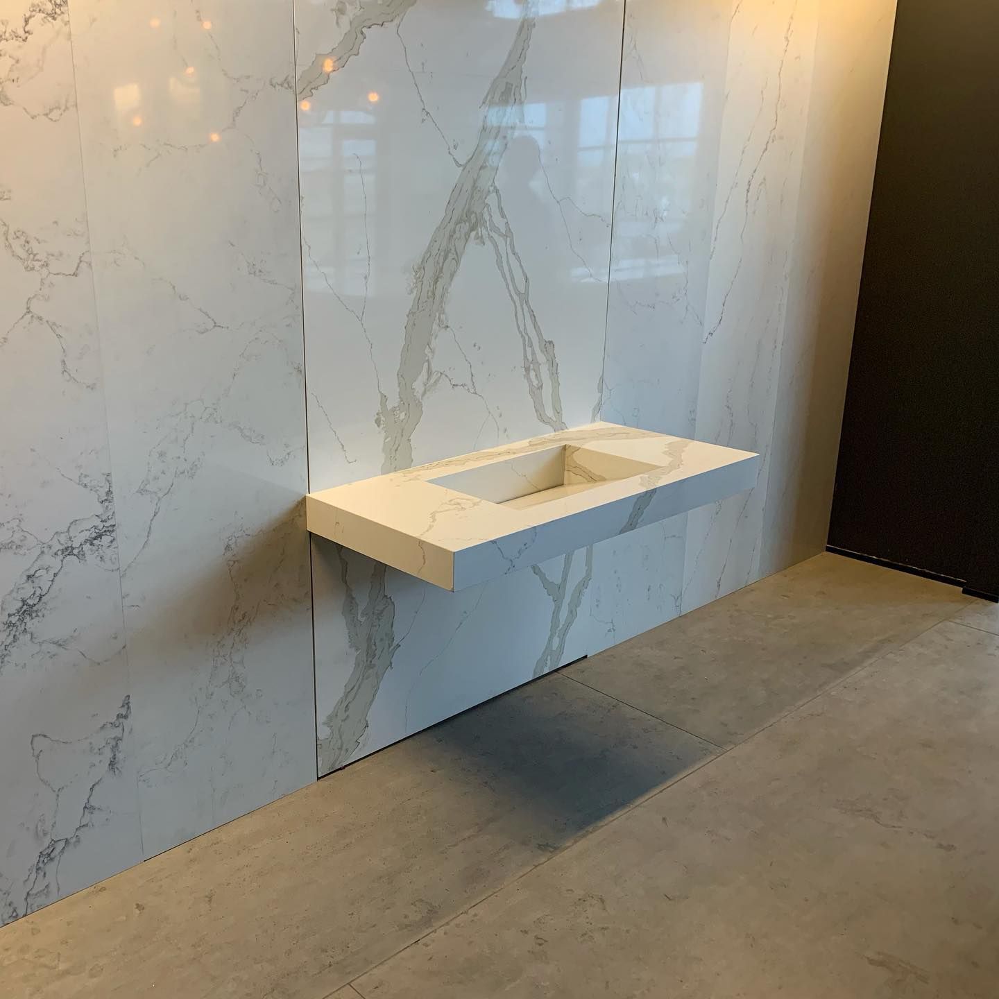 Floating white quartz sink on a marble-veined wall in a bathroom showroom.