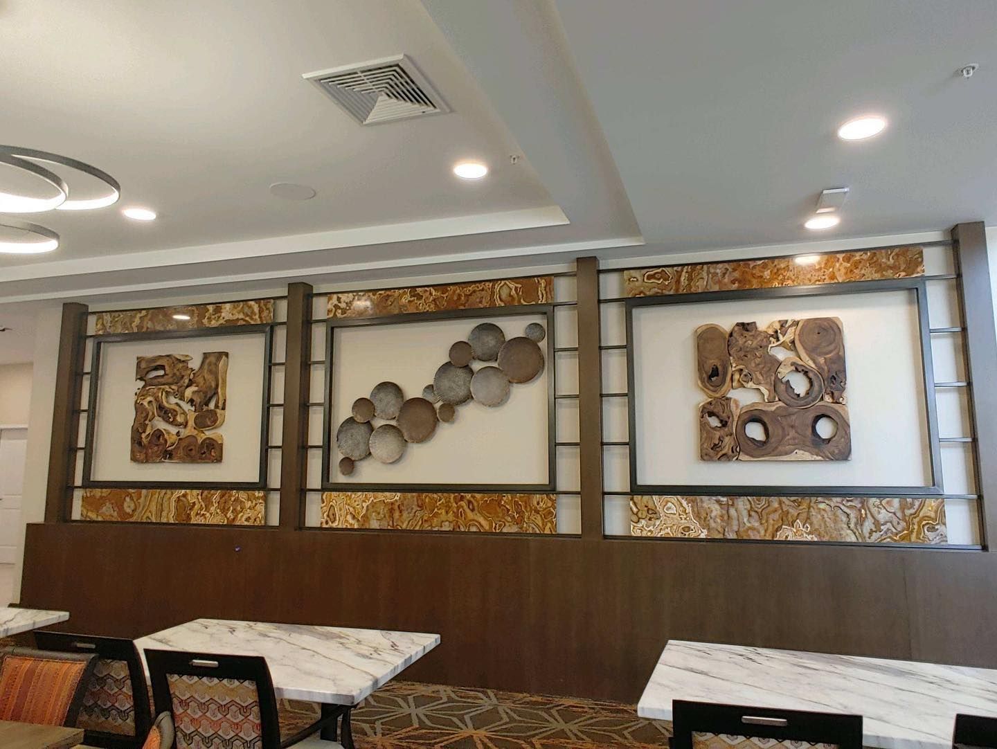 Dining area with tables and art: framed wood and metal sculptures above a wood panel wall.