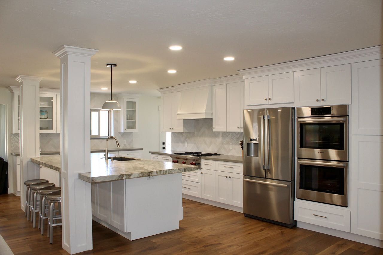 Modern white kitchen with island, stainless steel appliances, and wood flooring.