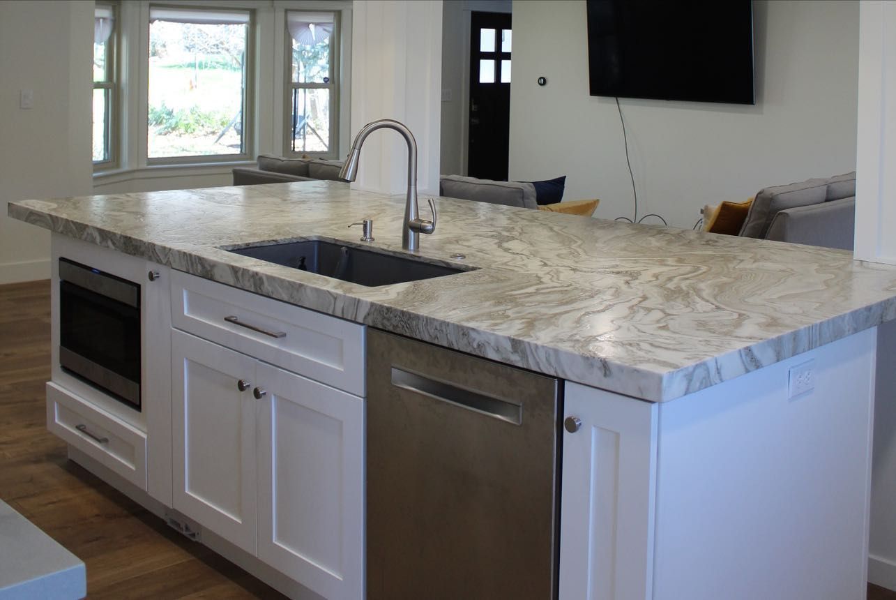 White kitchen island with stainless steel appliances and granite countertop.