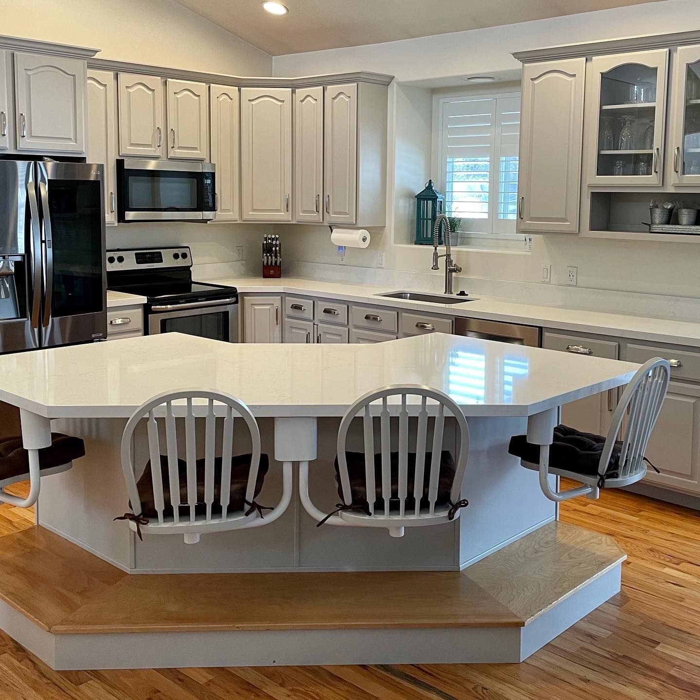 Kitchen with light gray cabinets, white countertops, island with seating, and stainless steel appliances.