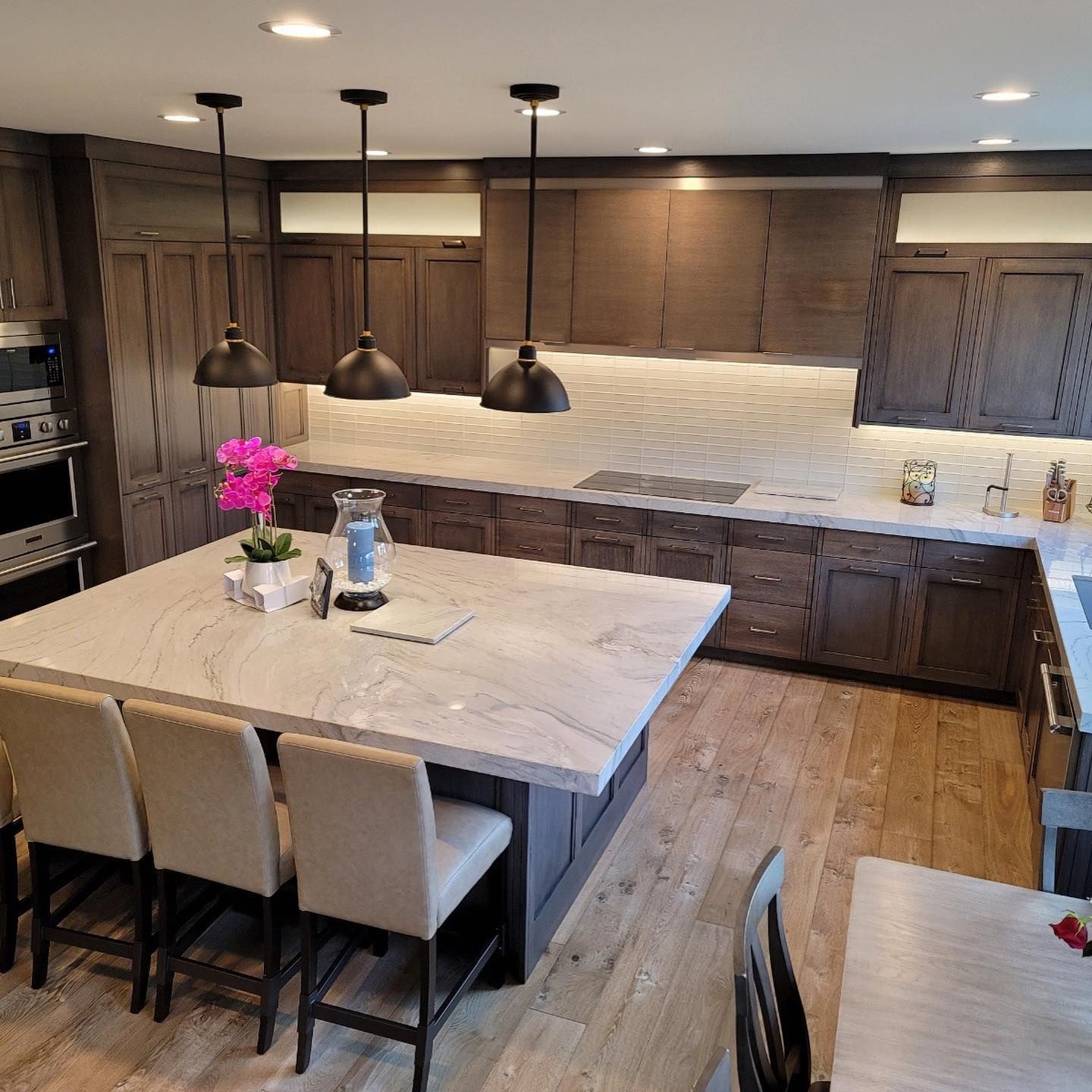 Modern kitchen with island, dark wood cabinets, white countertops, three pendant lights.
