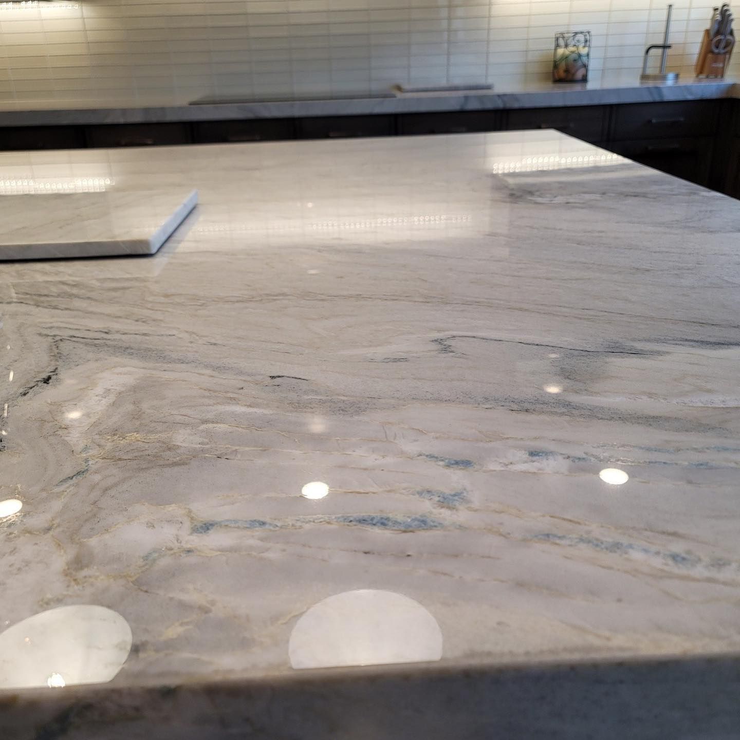 Close-up of a marble countertop with white, gray, and blue veining. Bright lights reflect on the glossy surface.