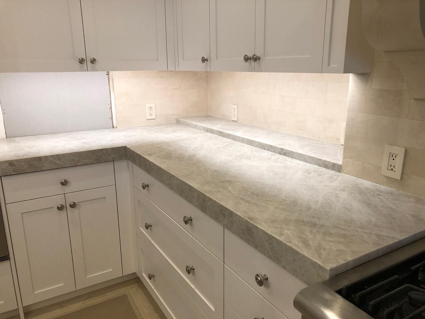 White kitchen with gray countertops and cabinets. Under-cabinet lighting illuminates the backsplash.