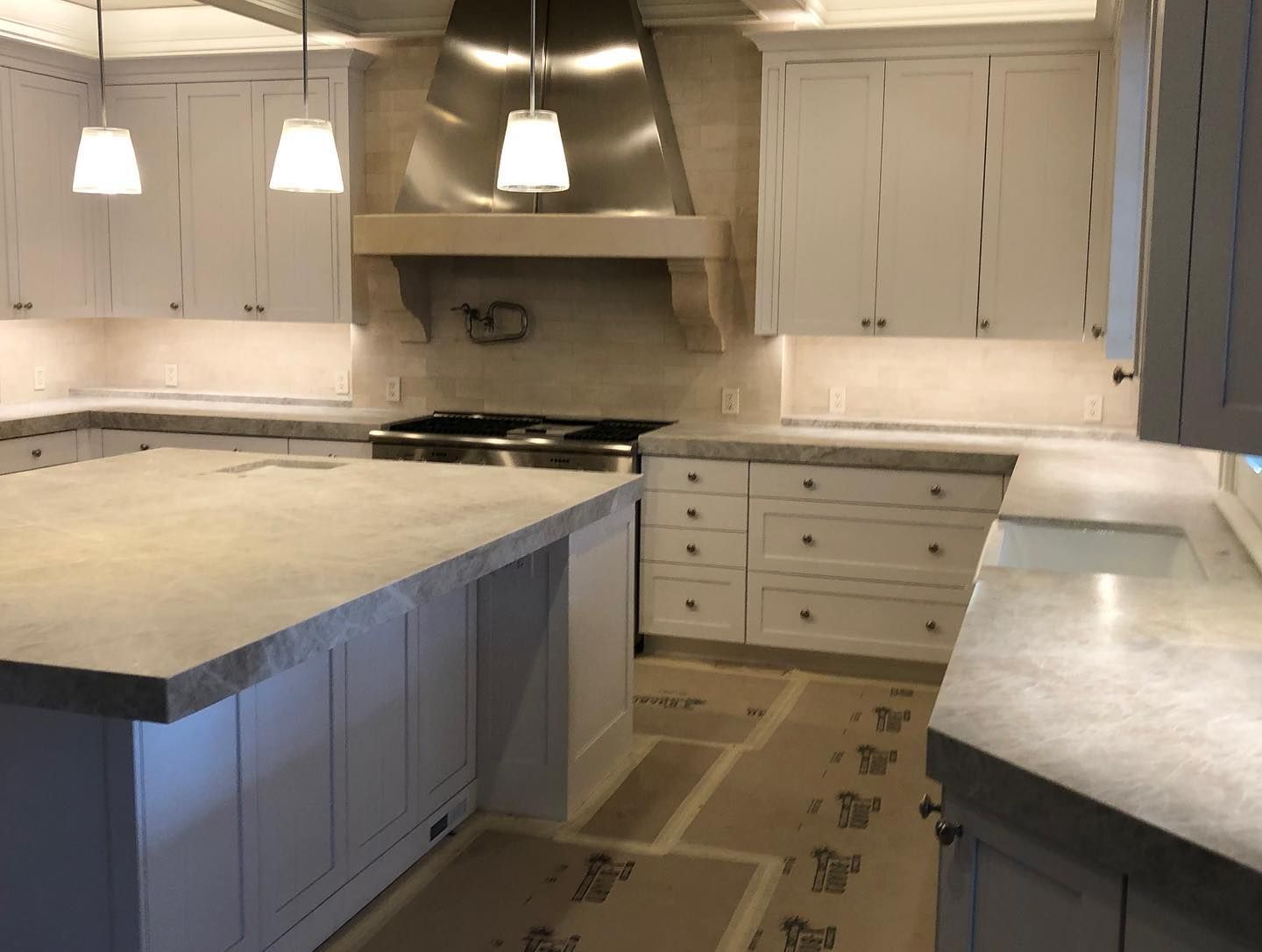 White kitchen with island, cabinets, range, and stainless steel hood. Gray countertops and flooring.