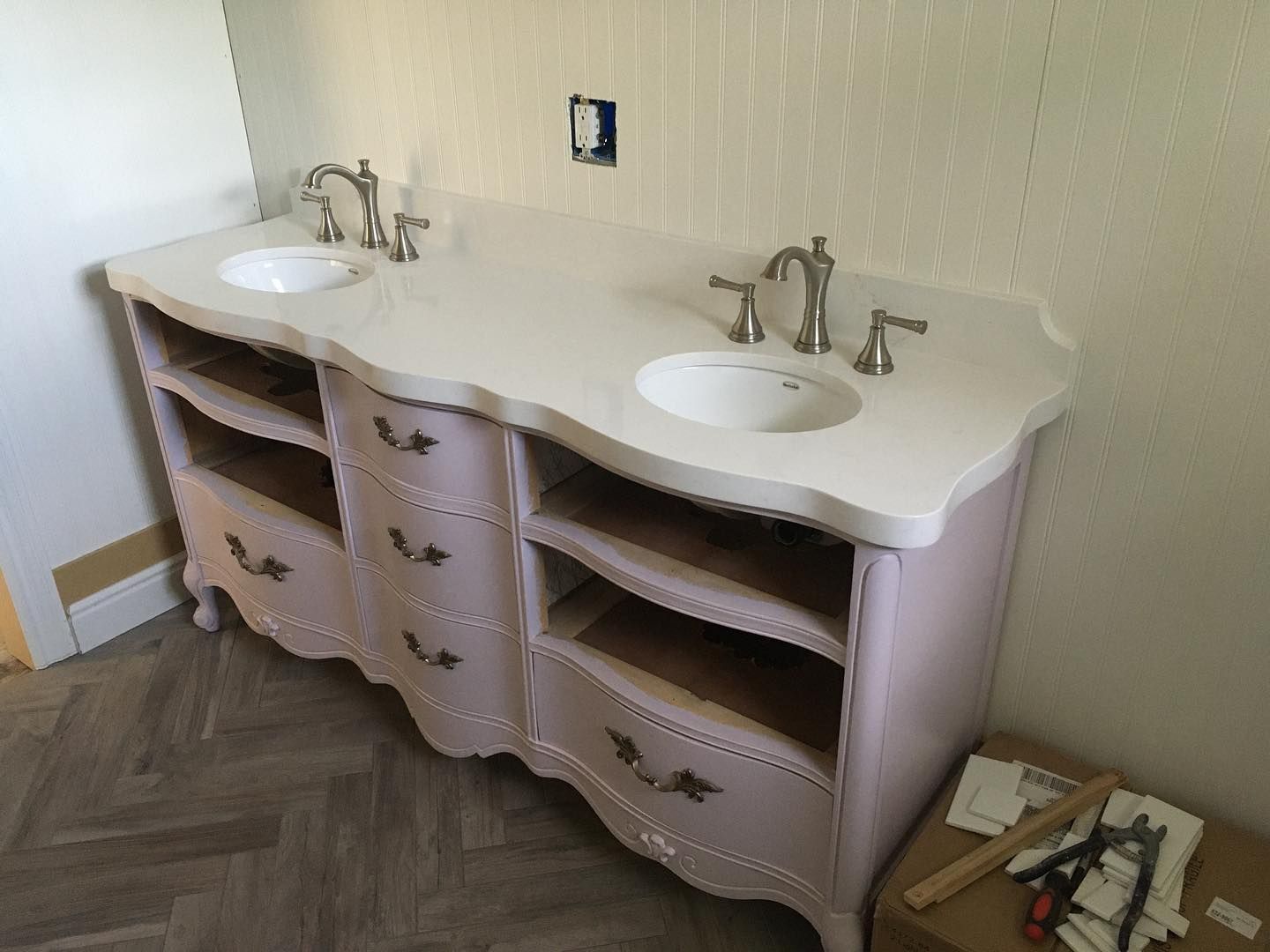 Pink double vanity with light countertop and two sinks, installed against a textured wall.