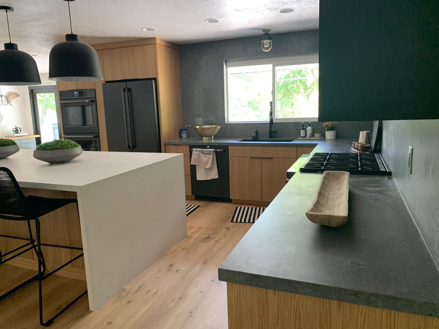Modern kitchen with light wood cabinets, dark countertops, and a white island with black pendant lights.