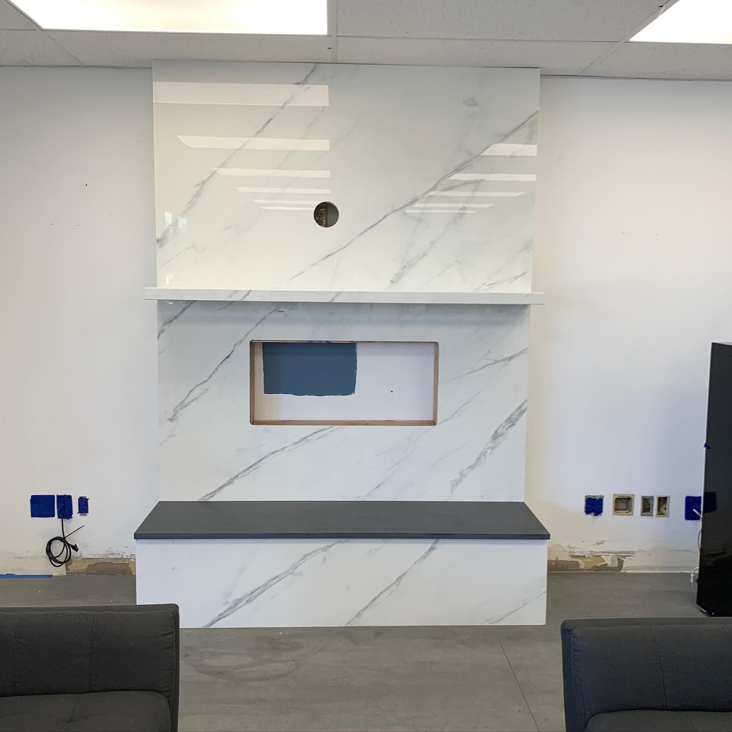Fireplace with marble-patterned tile, wooden mantel, and a bench. Unfinished walls and wiring visible.