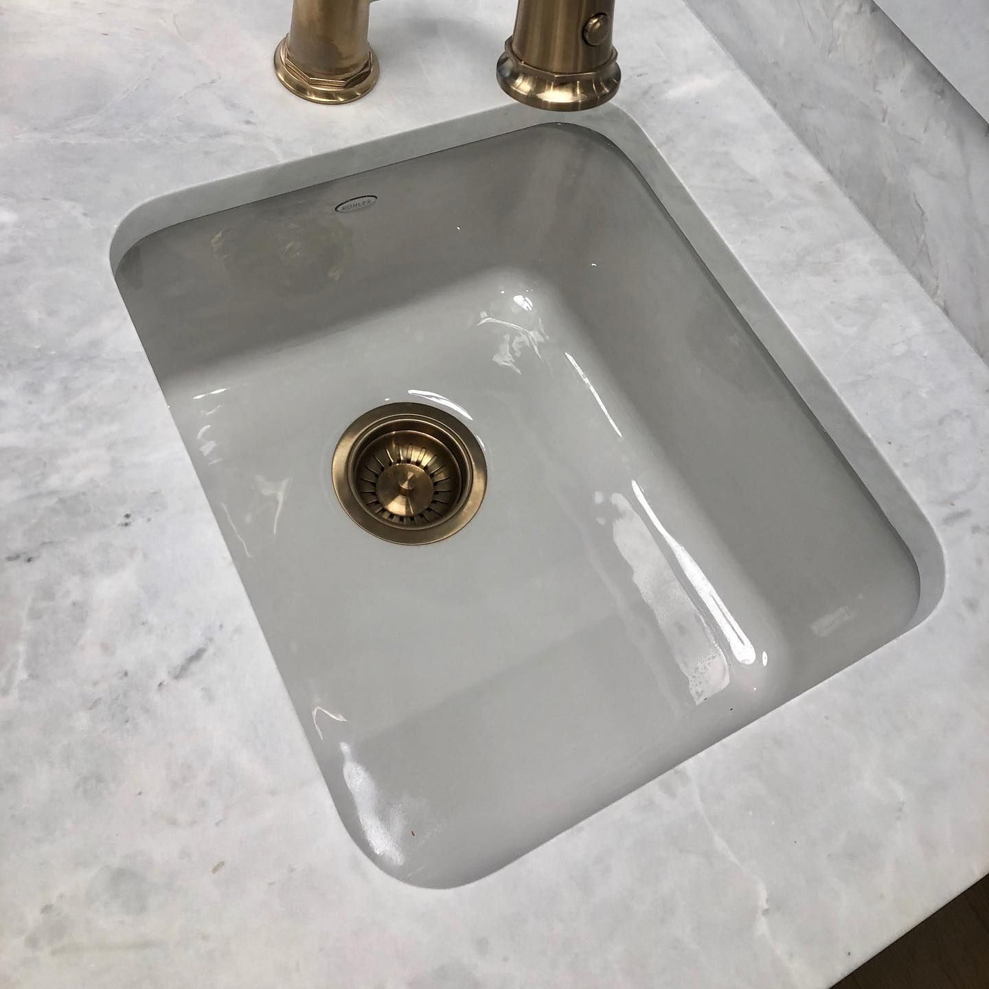 White rectangular sink in a marble countertop with a brass faucet.